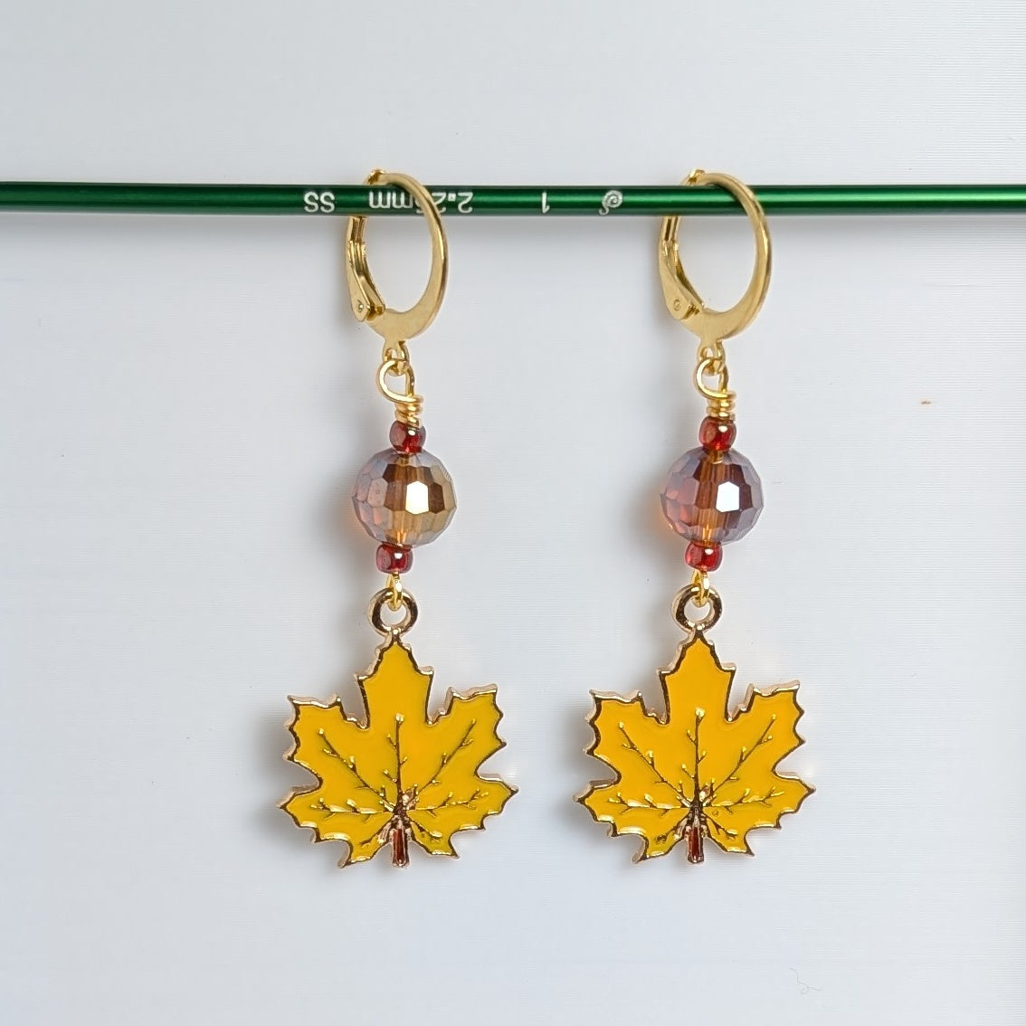 Yellow leaf earrings with gold hooks and beads on a white background