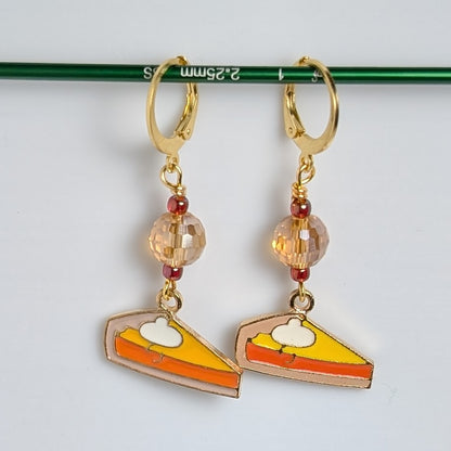 Pair of earrings with pie slice charms on a white background
