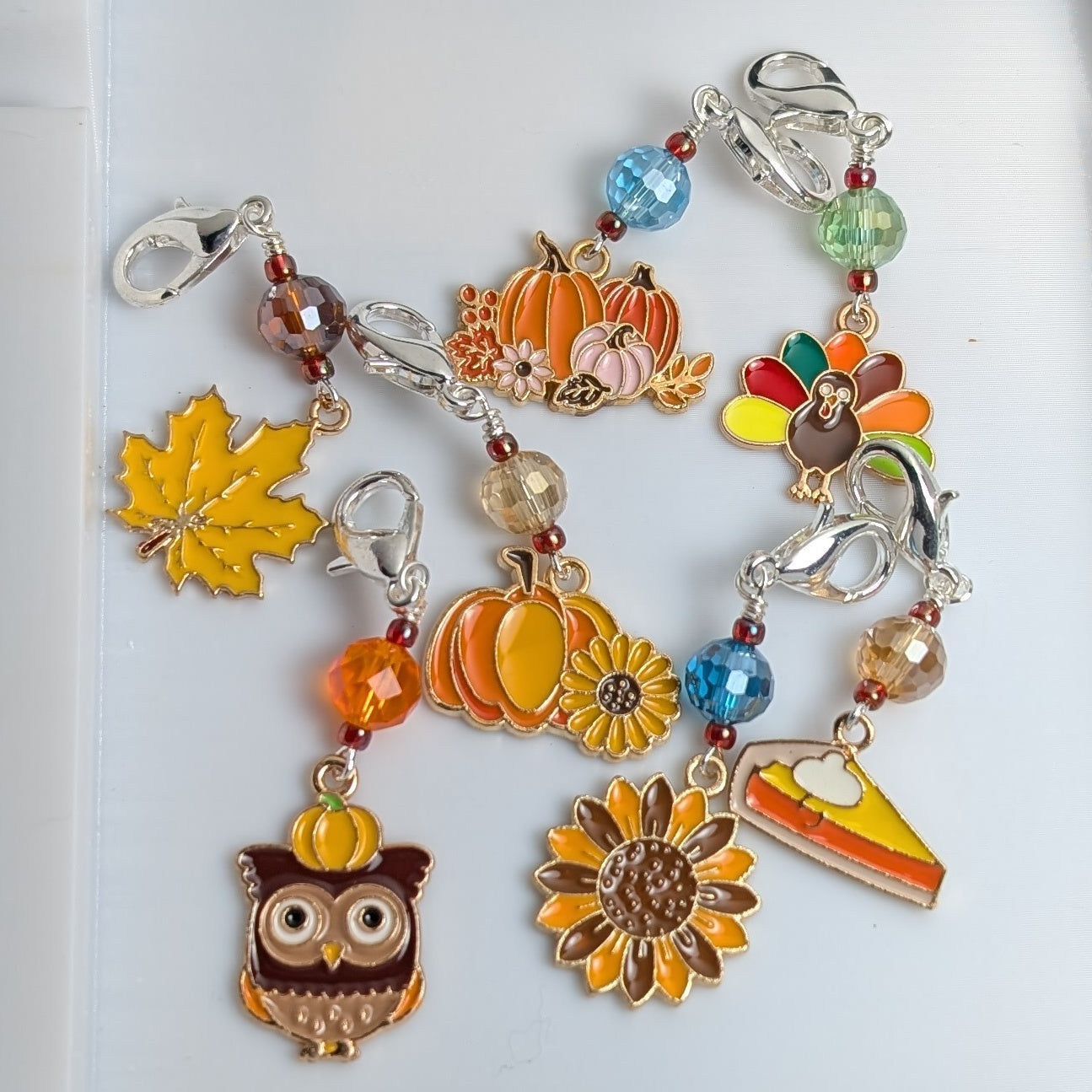 Colorful stitch markers with autumn-themed charms on a white background