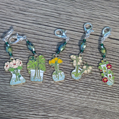 Set of five decorative stitch markers with plant and flower designs on a wooden surface.