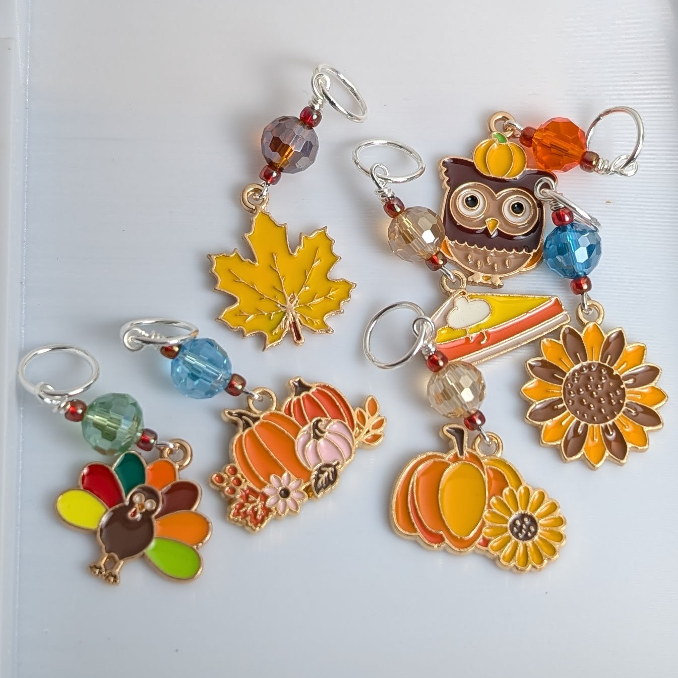 Colorful stitch markers with autumn-themed designs on a white background