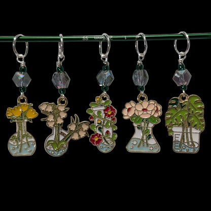 Set of five floral-themed stitch markers charms on a green rod against a black background