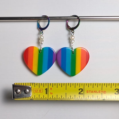 Rainbow heart-shaped earrings with a Stanley measuring tape for scale on a white background
