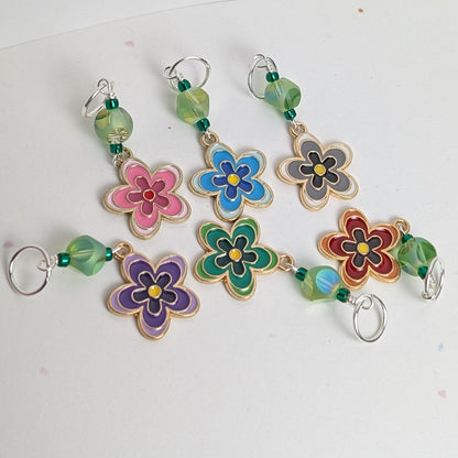 Colorful flower-shaped stitch markers with beads on a white background